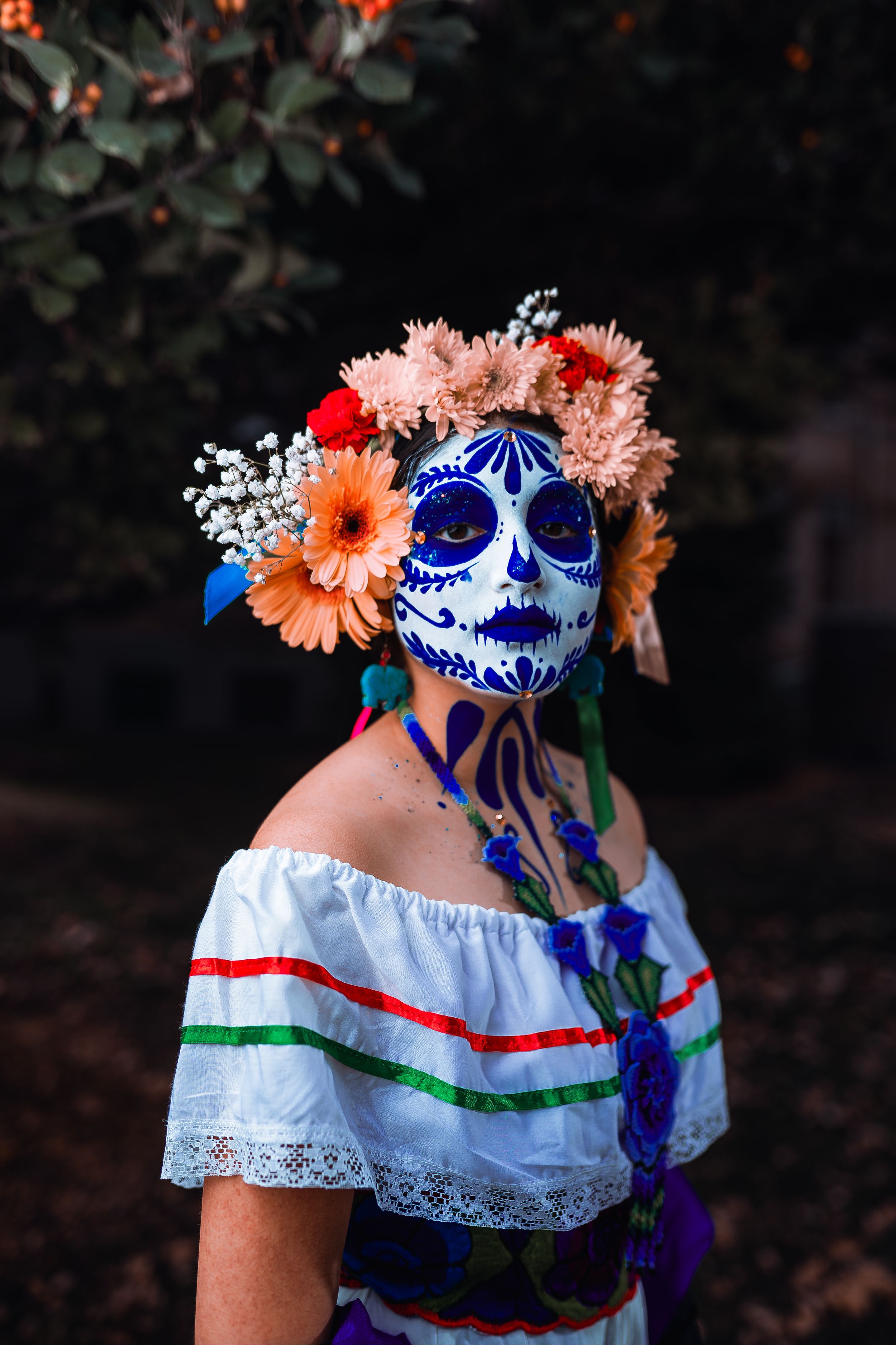 Day of the Dead mask decorated with blue patterns and floral crown featuring orange and pink flowers.
