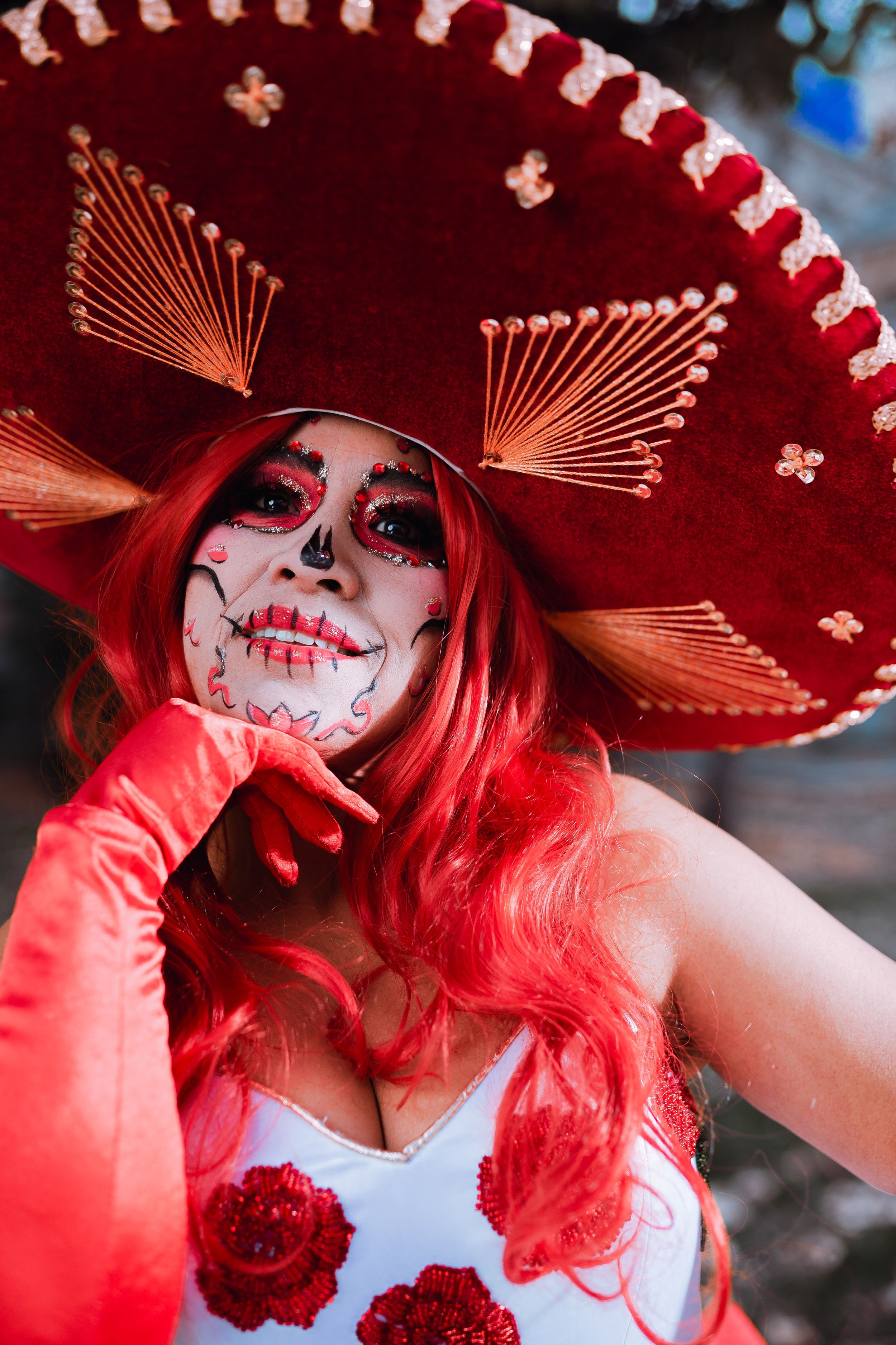 Artistic portrait showing detailed sugar skull makeup under ornate red sombrero with fan details.