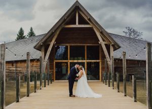 A wedding couple posing in front of a rustic wooden chapel with timber frame details.