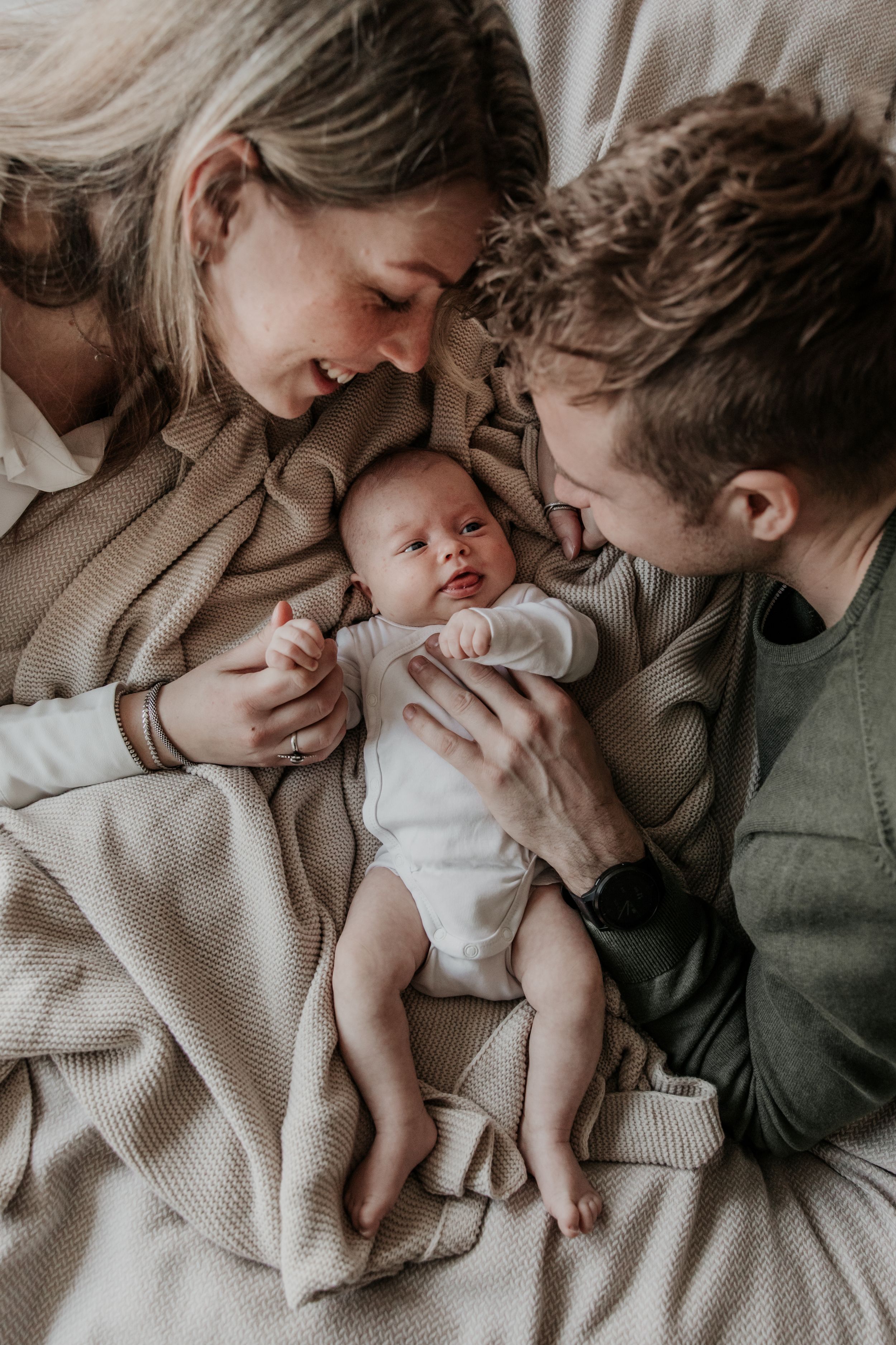 Papa en mama op bed met hun newborn houden handjes vast