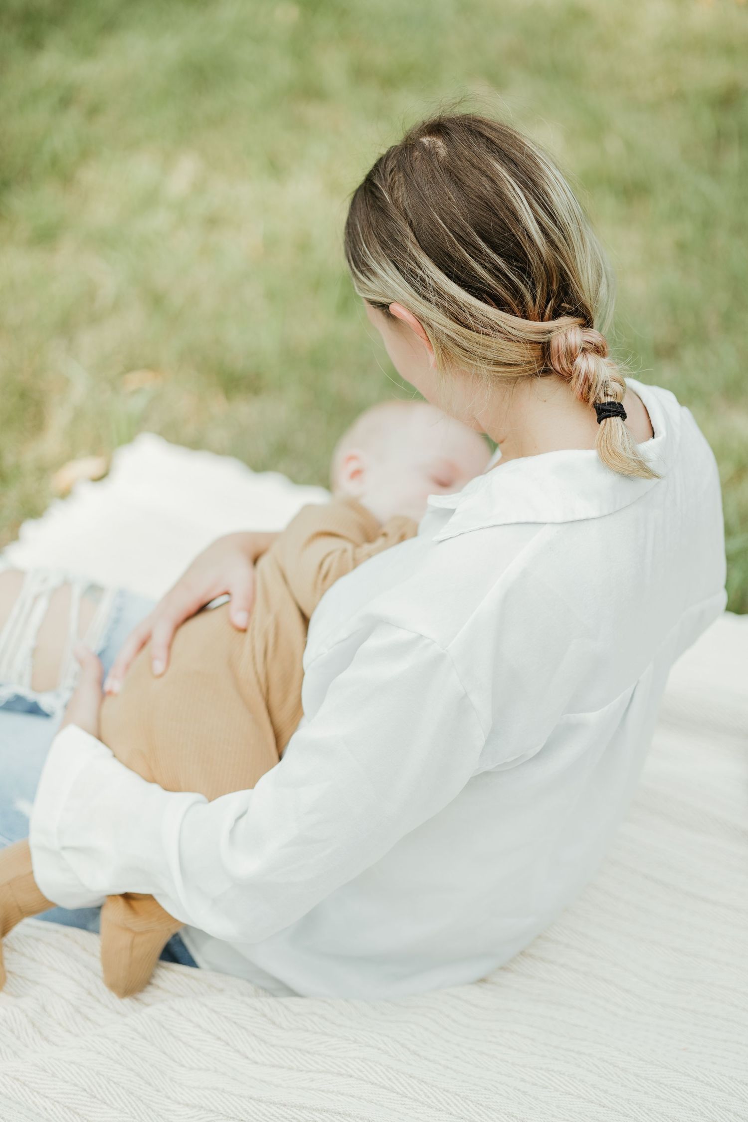 Tender parenting moment on white blanket outdoors in natural setting.