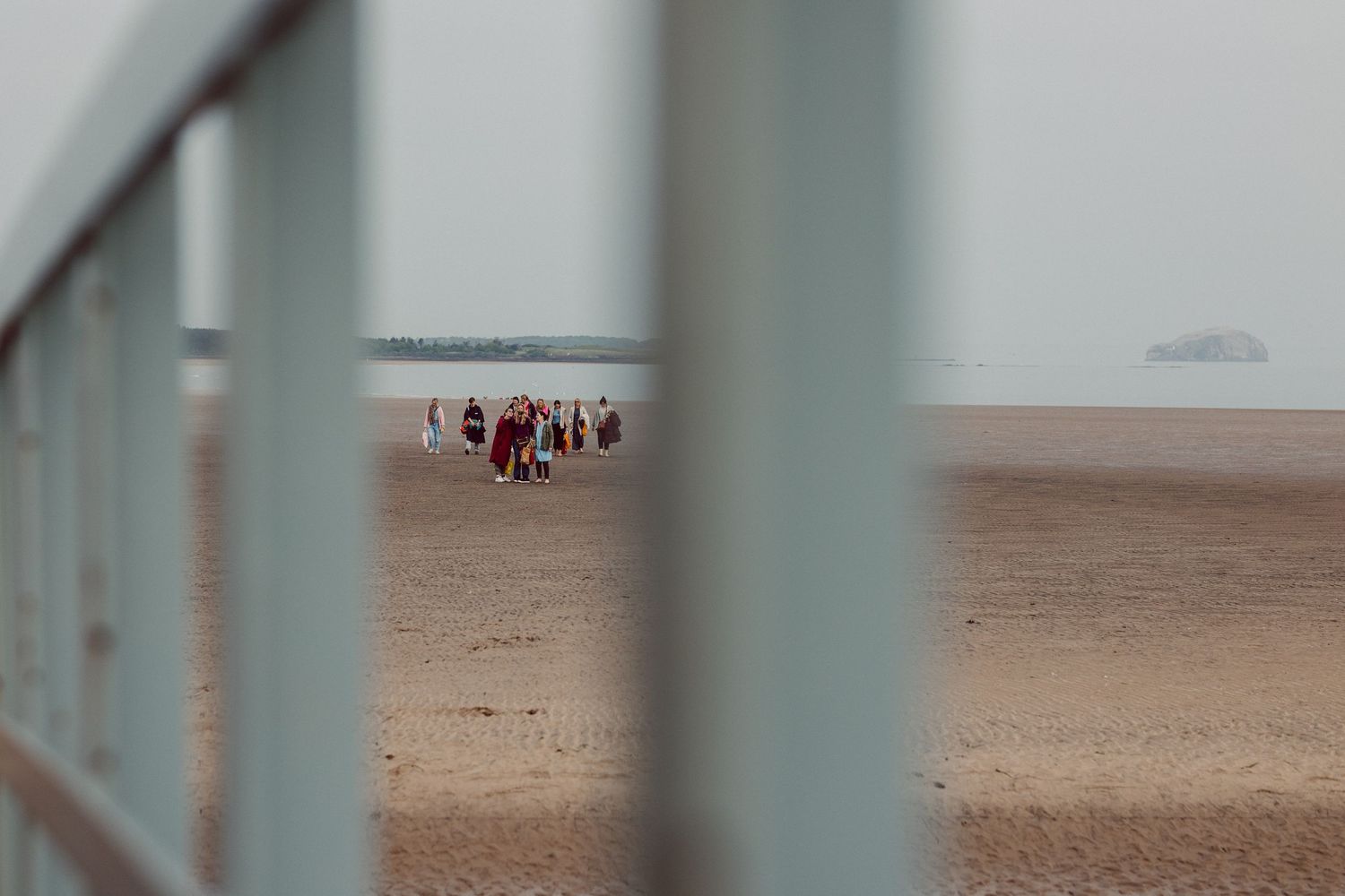 View through railings of people walking on distant beach.