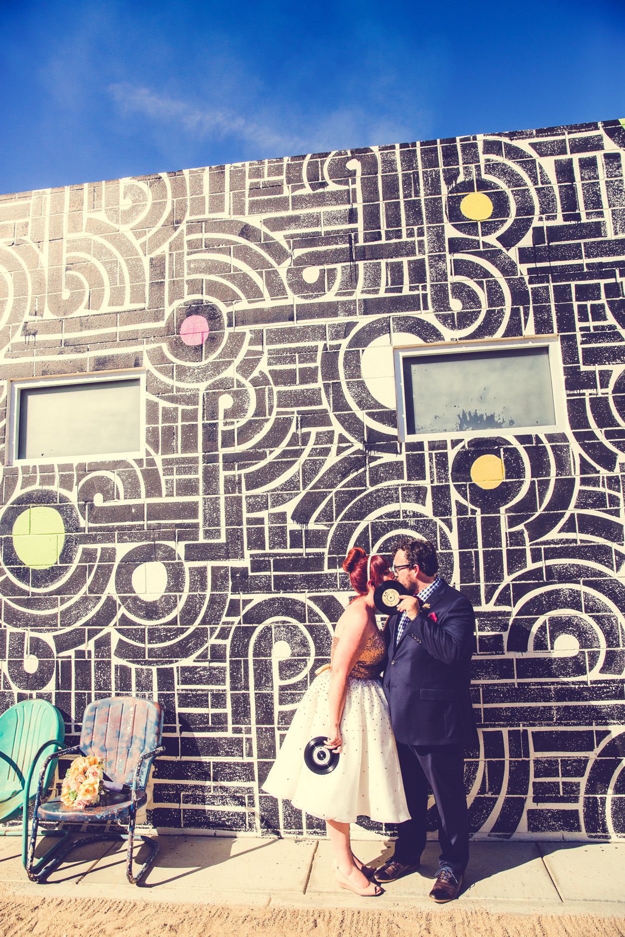 Couple poses against geometric wall mural with circles and lines in urban setting.