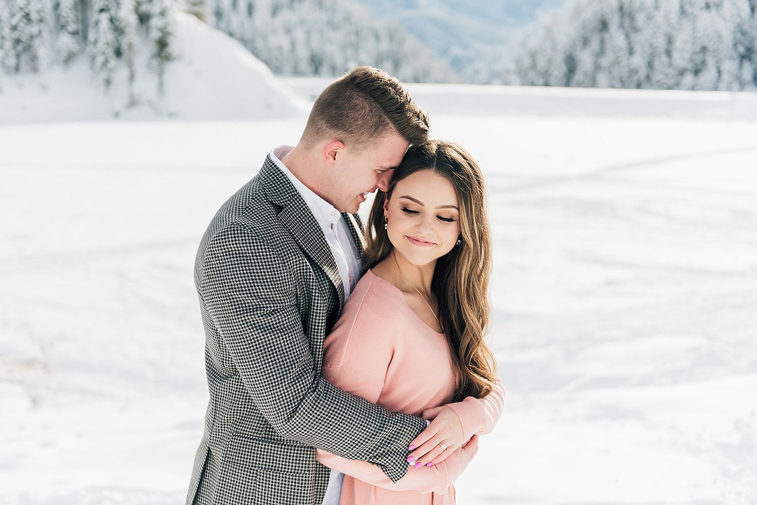 Intimate winter portrait of couple embracing in snow-covered mountain landscape.