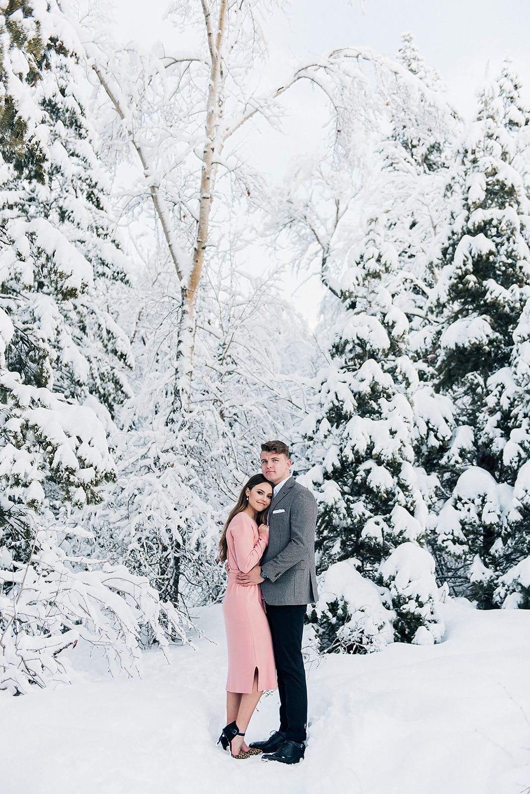 Couple shares intimate moment in winter wonderland setting with snow-covered trees.