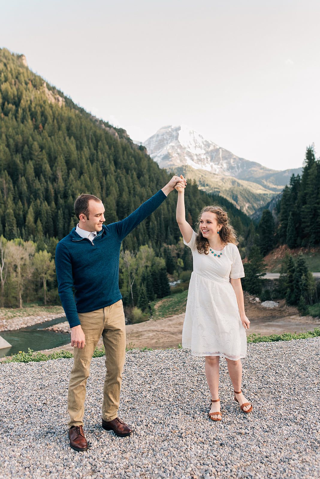 A couple dances and twirls together on a mountain overlook with snow-capped peaks in the distance.