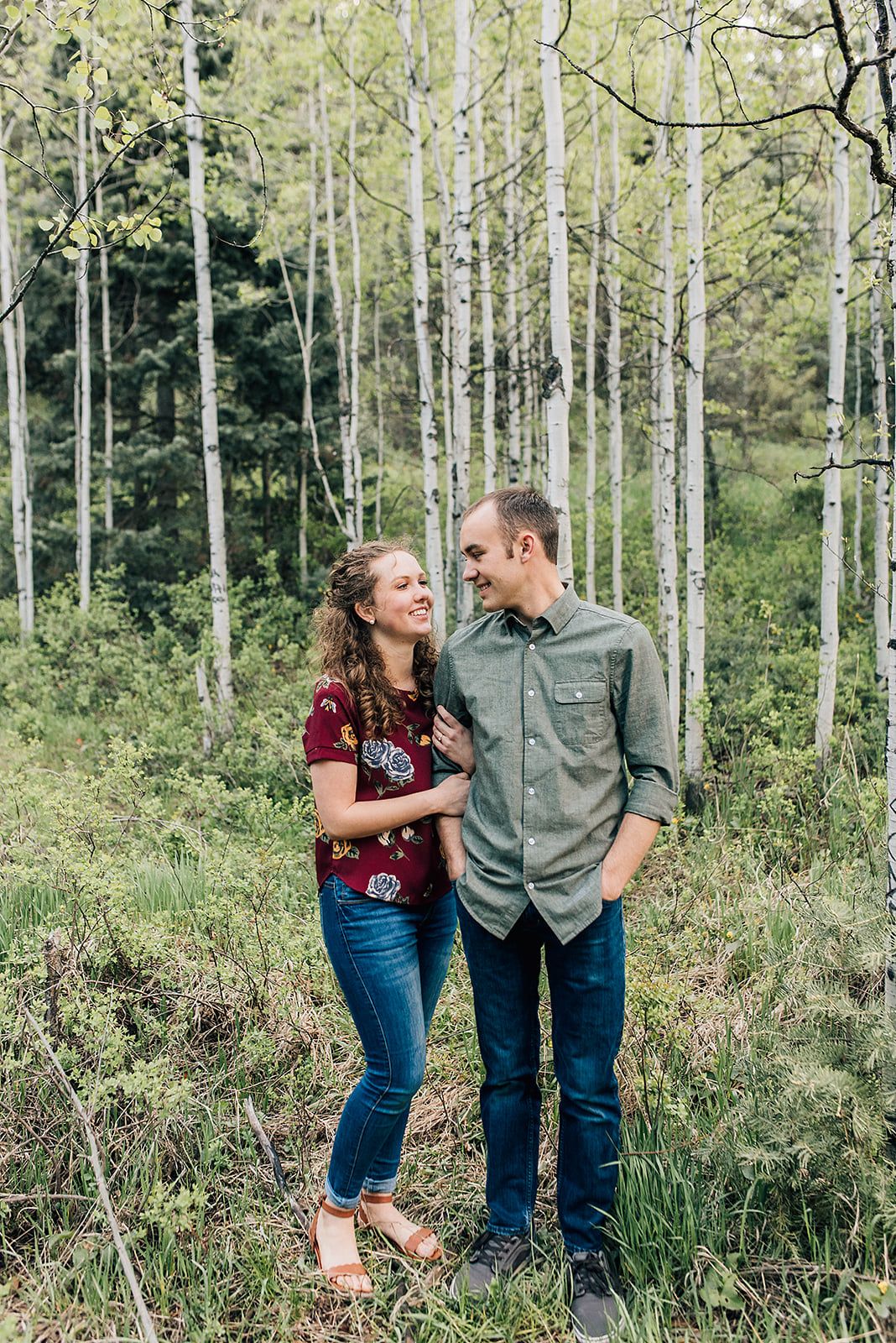 A couple shares a romantic moment among tall white aspen trees in a summer forest.