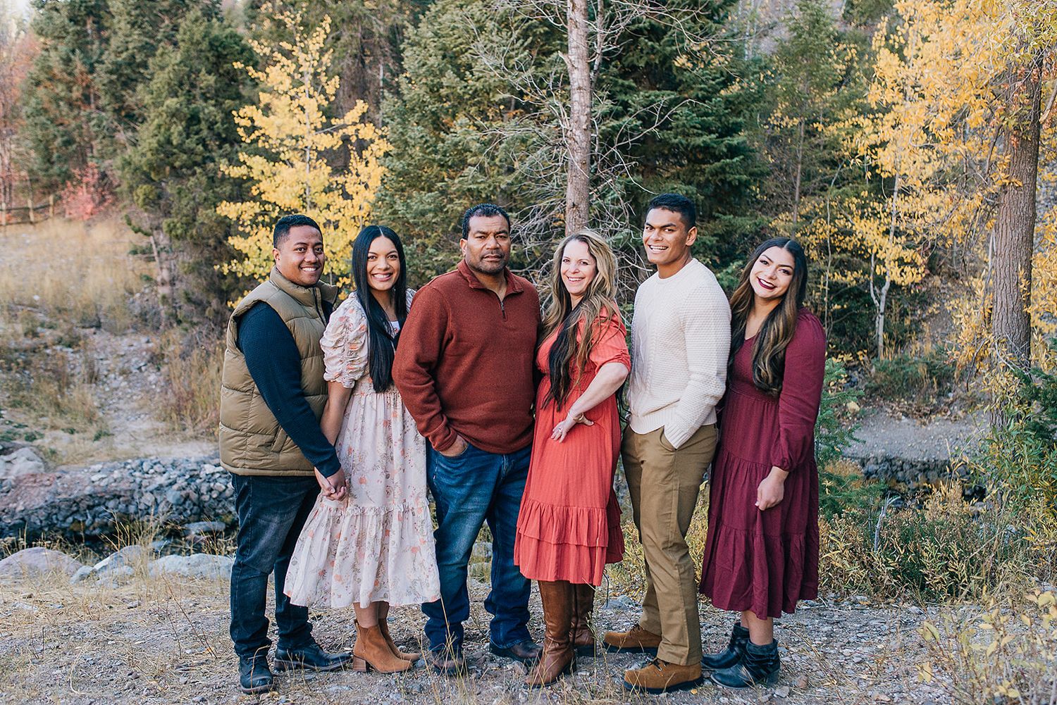 Group in coordinated fall outfits poses together in front of autumn trees and mountain scenery.