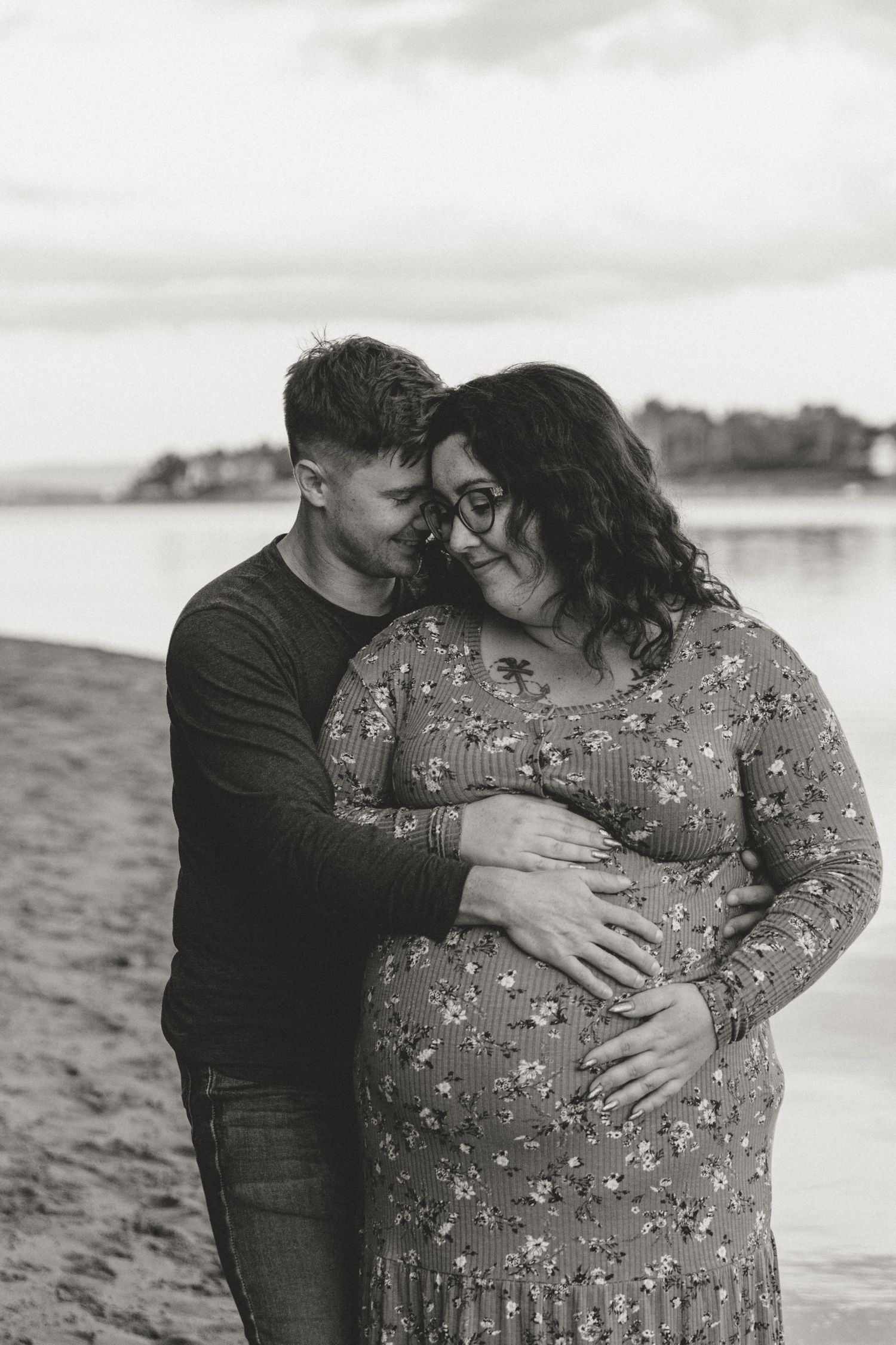 Intimate maternity portrait of couple embracing on beach in black and white.