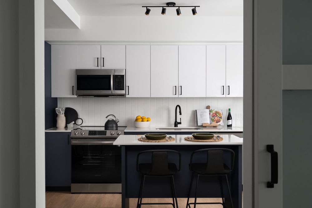 Modern kitchen with white upper cabinets, black base cabinets, and bar seating at a peninsula counter.