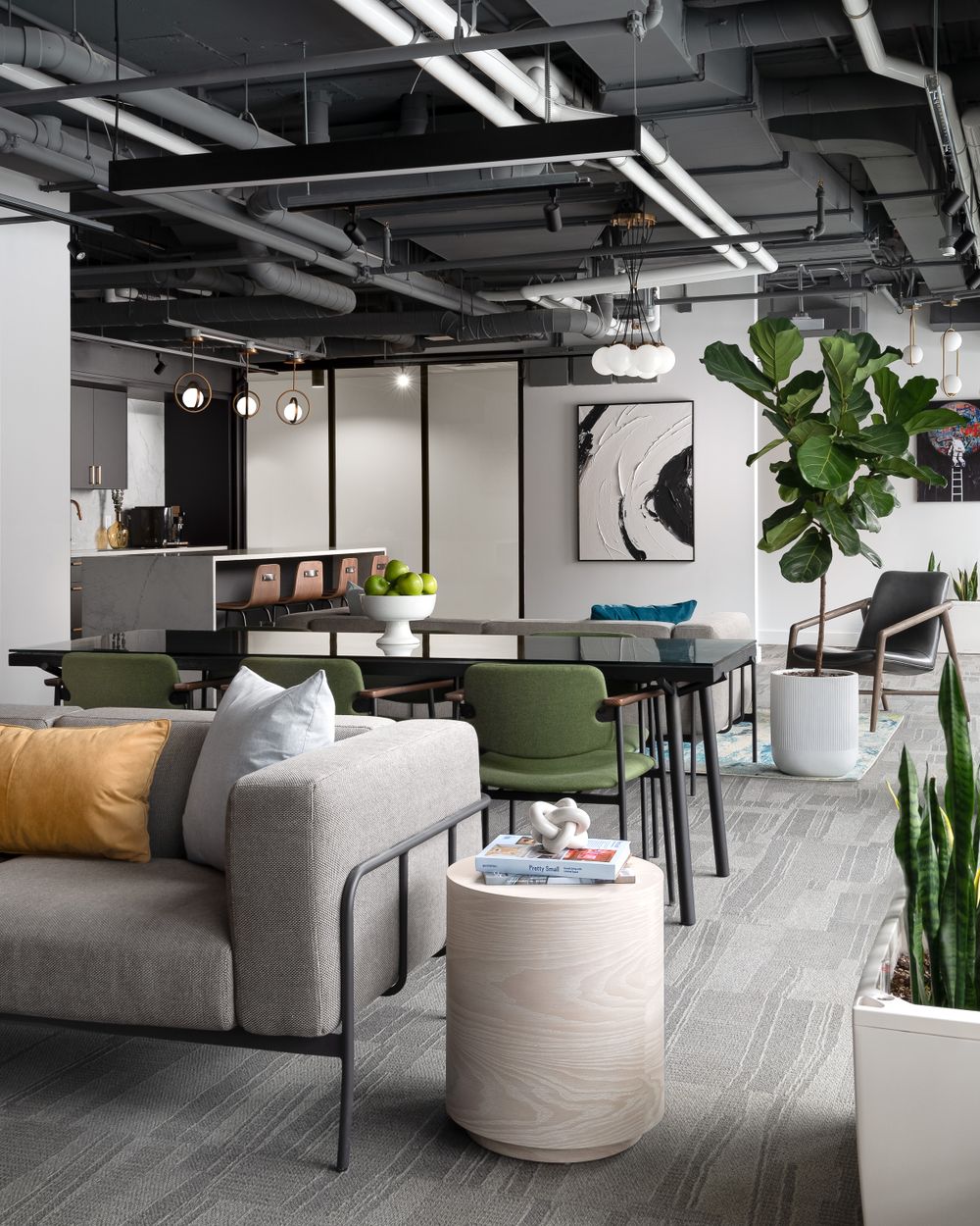 Modern office lounge with grey sofa, green chairs and industrial ceiling details.