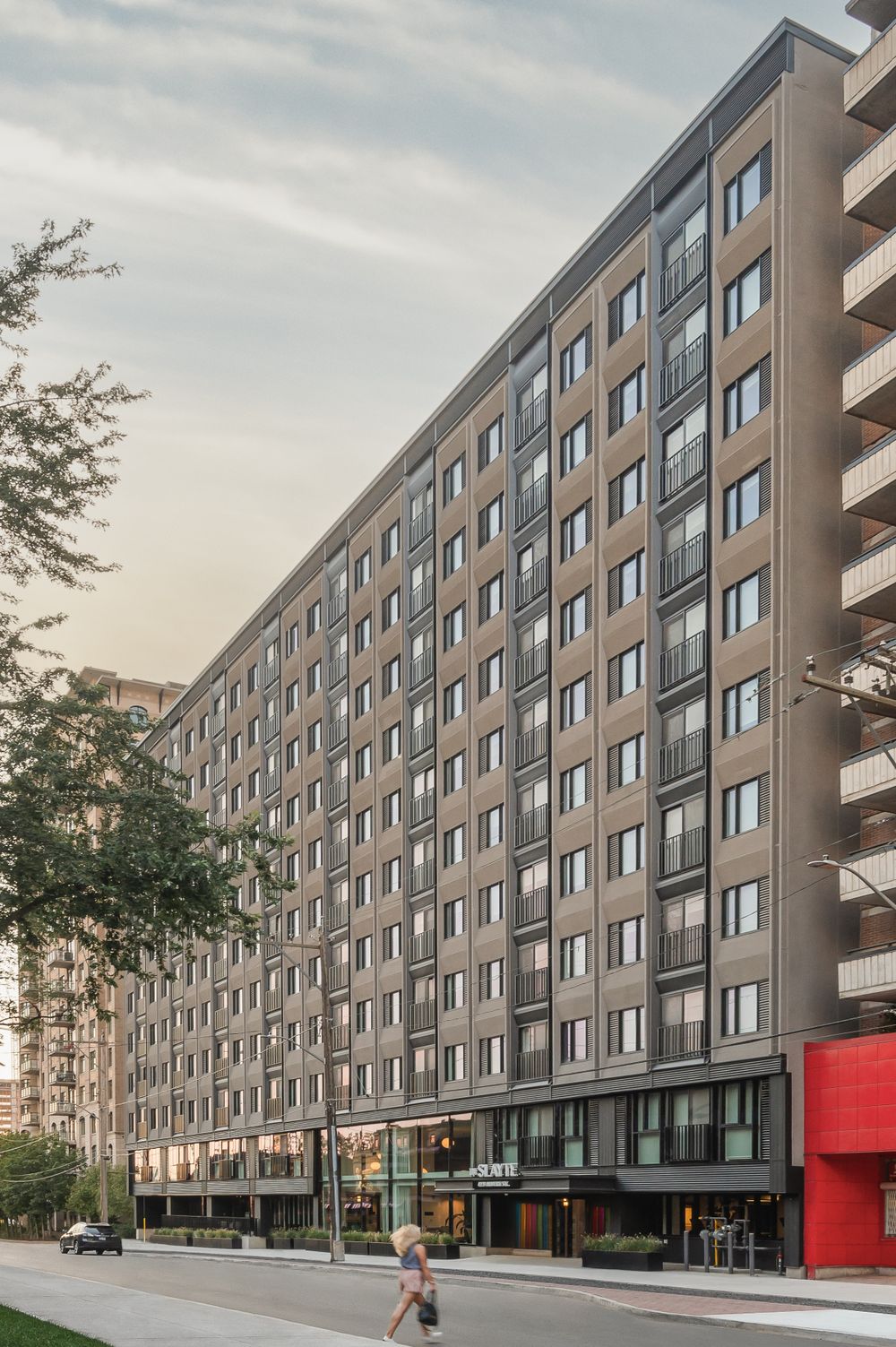 Modern multi-story apartment building with uniform windows and ground-floor retail space in urban setting.