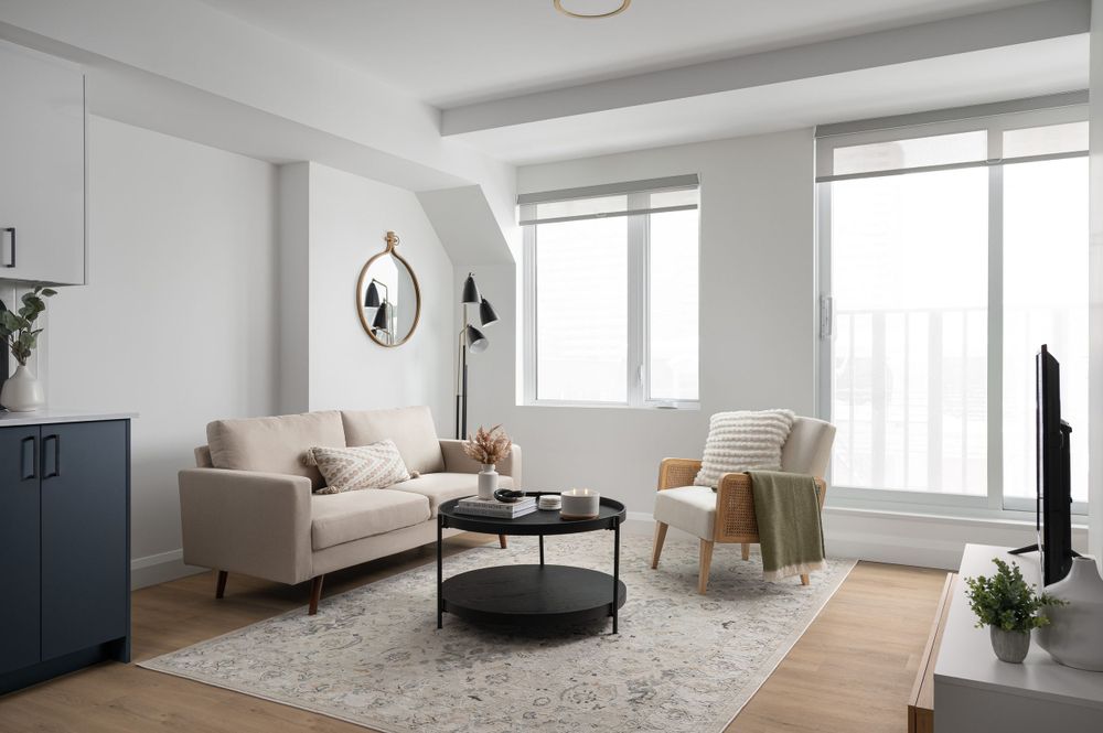 Contemporary living room with beige sofa, round coffee table, and large windows offering city views.