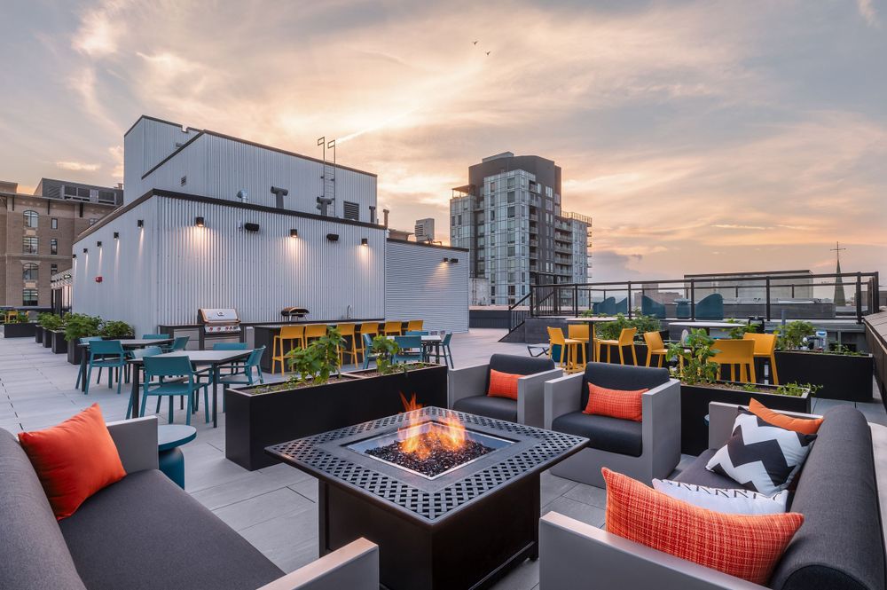 Stylish rooftop terrace with lounge seating, fire table, and colorful chairs under sunset sky.