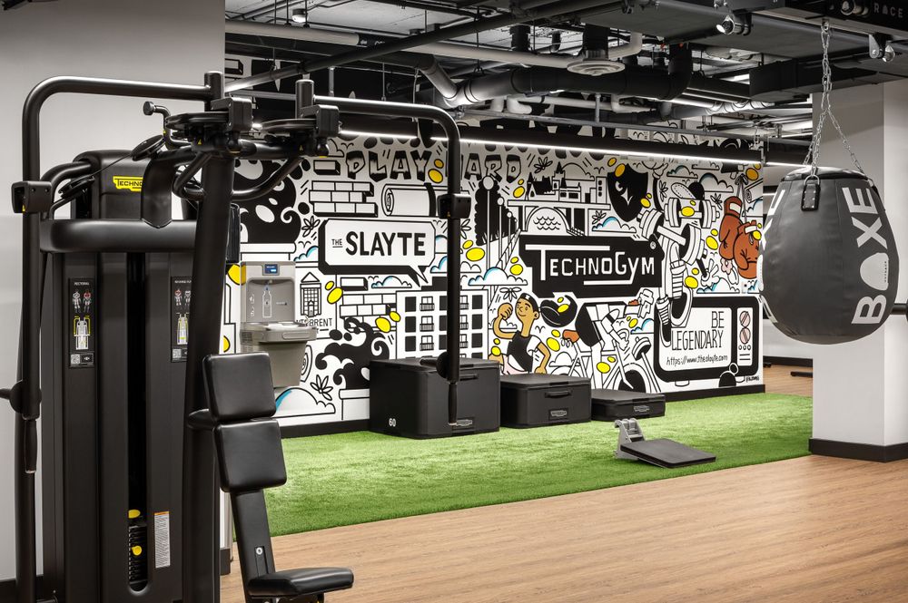 Modern gym facility with exercise equipment and graffiti-style wall art on artificial turf flooring.