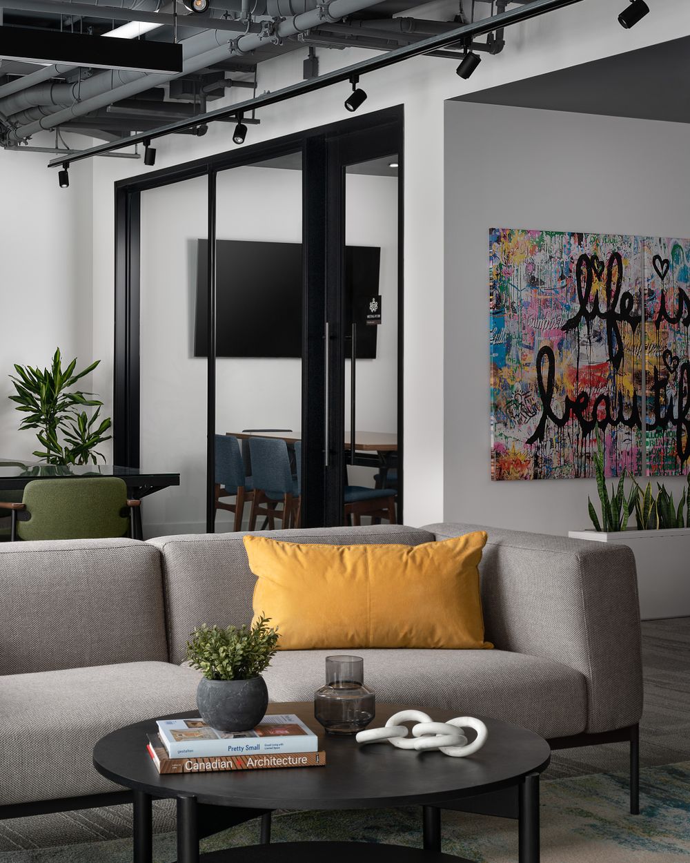 Modern office space with grey sofa, colorful wall art, and industrial ceiling details.