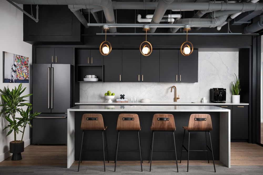 Contemporary black kitchen with wooden bar stools and pendant lighting in an open office space.