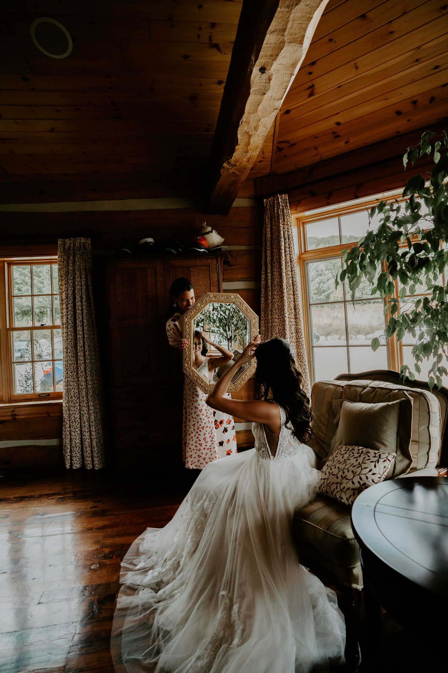 Bride getting ready with maid of honour holding mirror