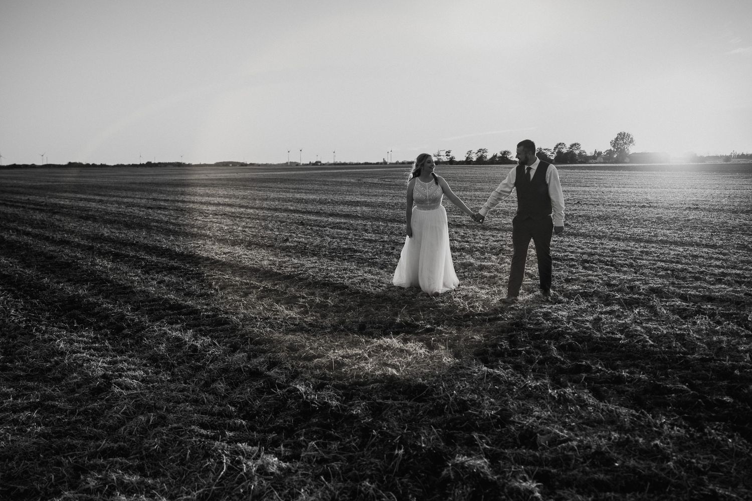 bride and groom hold hands walking through cultivated field