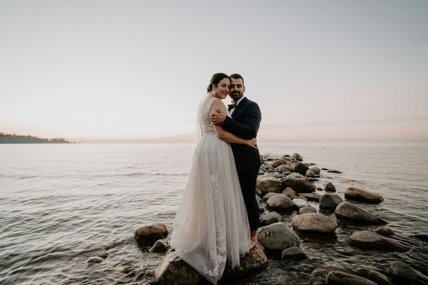 bride and groom standing on rocks at Lake Huron