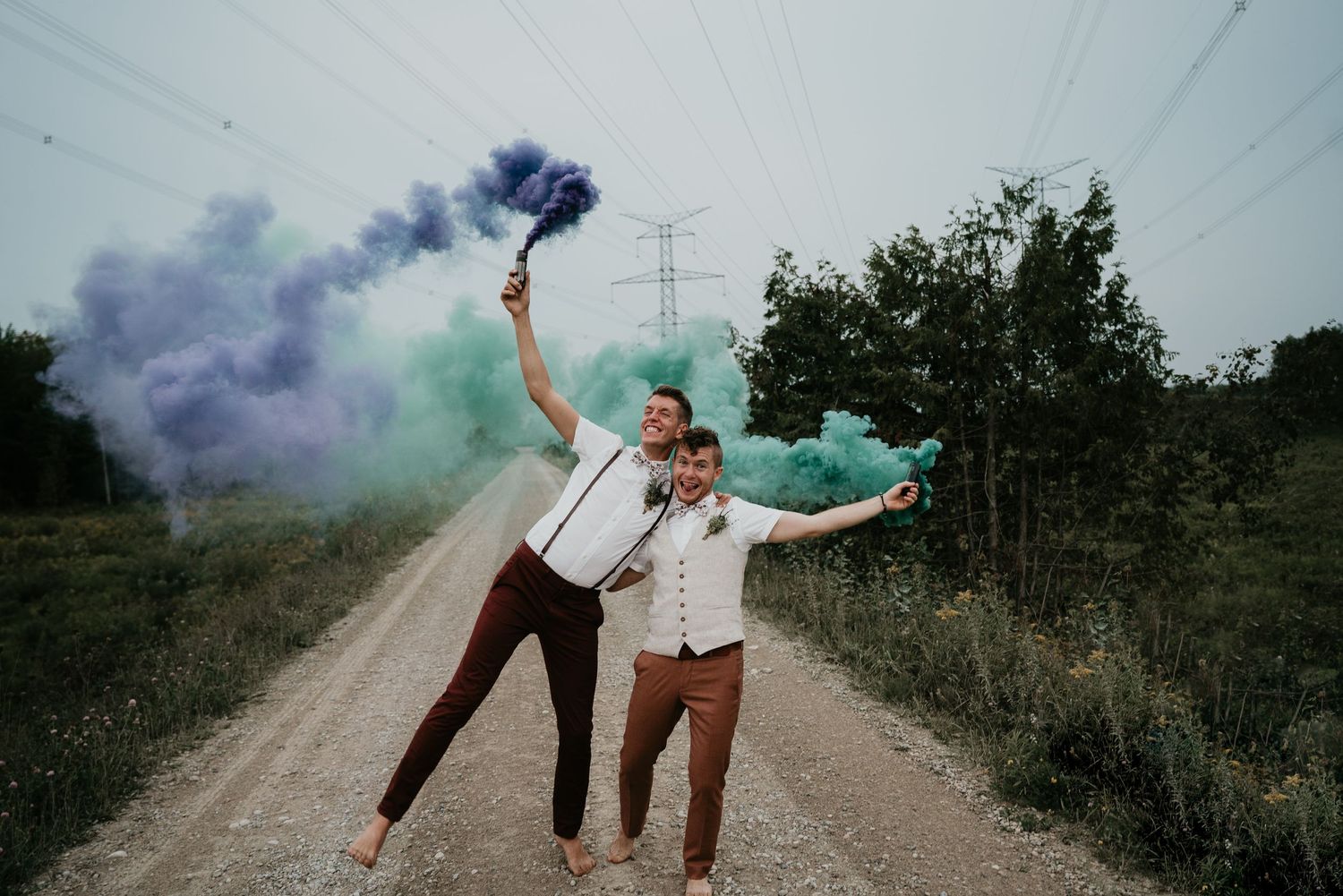 groom and groom running down road with green and blue coloured smoke