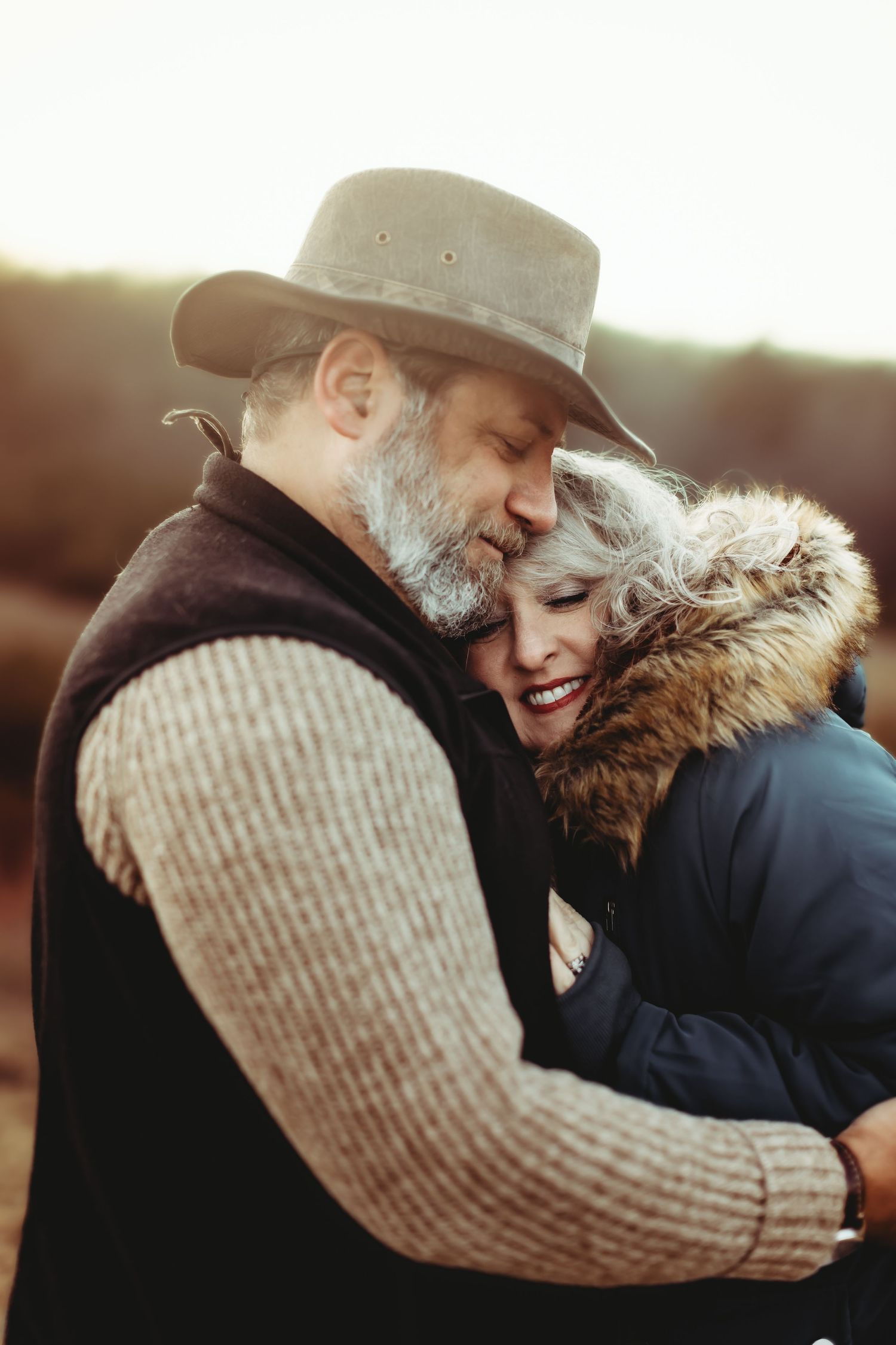 A couple embraces outdoors wearing winter clothing with a knit sweater and fur-lined coat.