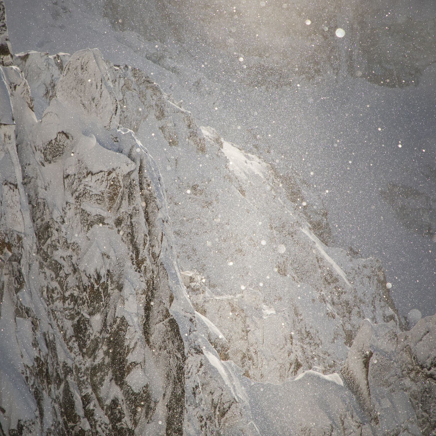 Snow-covered rocky mountain face with jagged edges and natural textures visible in grey tones.