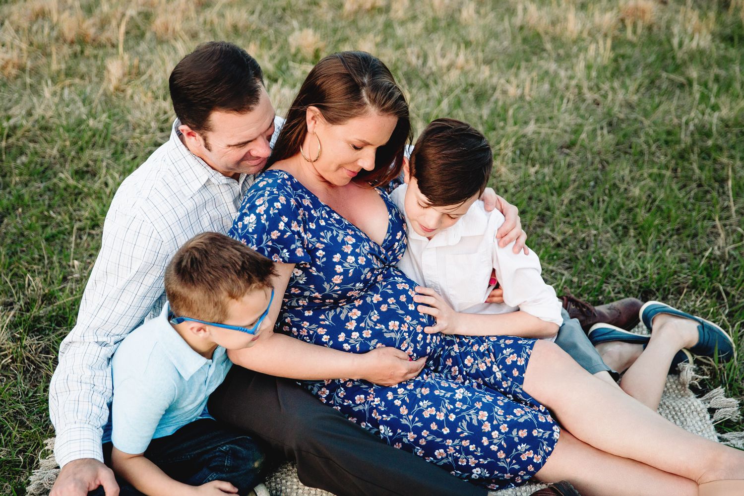 family sitting on blanket in grass by kansas city maternity photographer