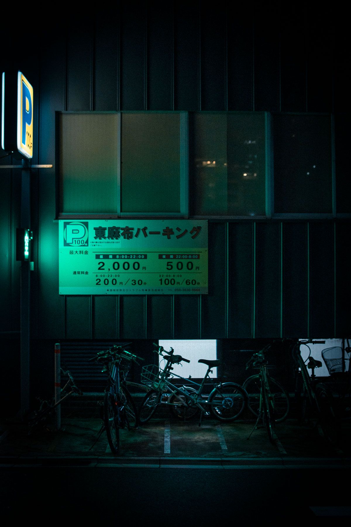 Bicycle parking sign and bikes silhouetted against green-tinted urban night scene.