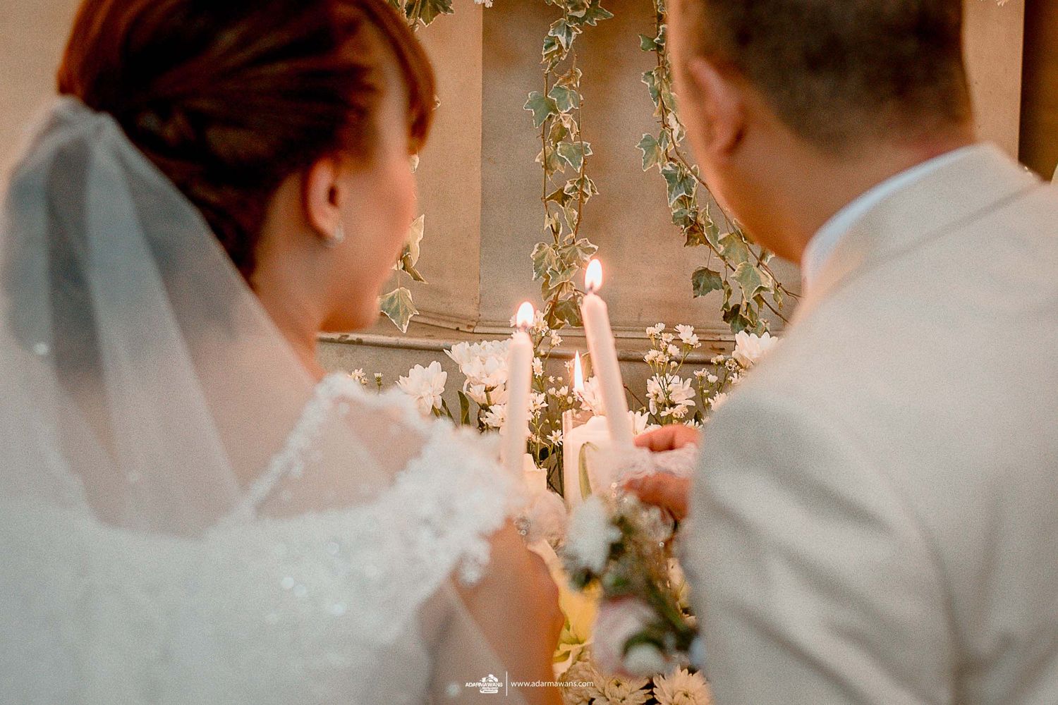 A couple lights unity candles surrounded by floral decorations during their wedding ceremony.