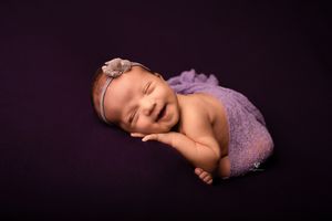 Smiling newborn girl wrapped in purple with purple backdrop in taco pose; newborn photography session; Lexington studio