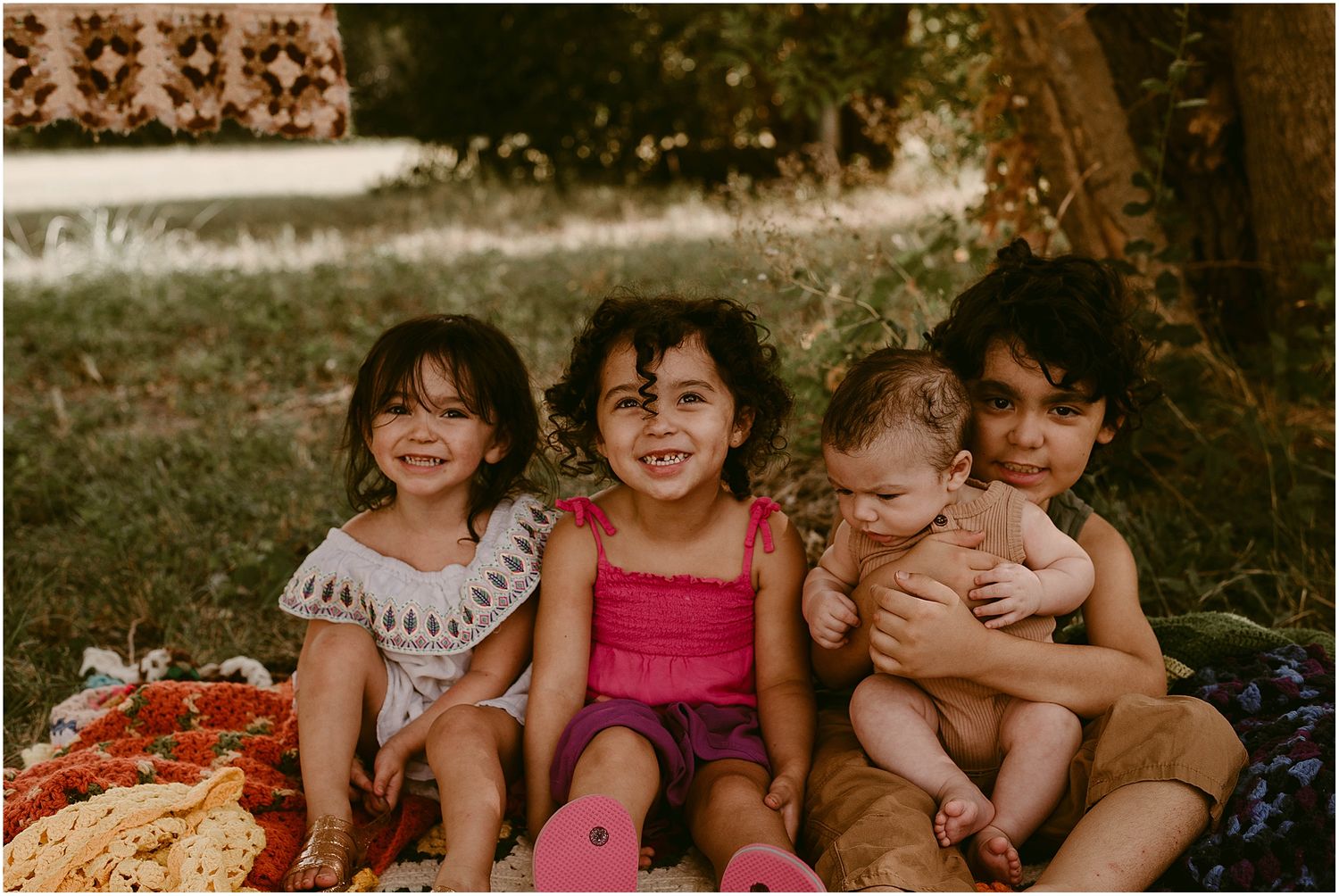 Group of children sitting together outdoors with vintage-style backdrop and warm lighting.
