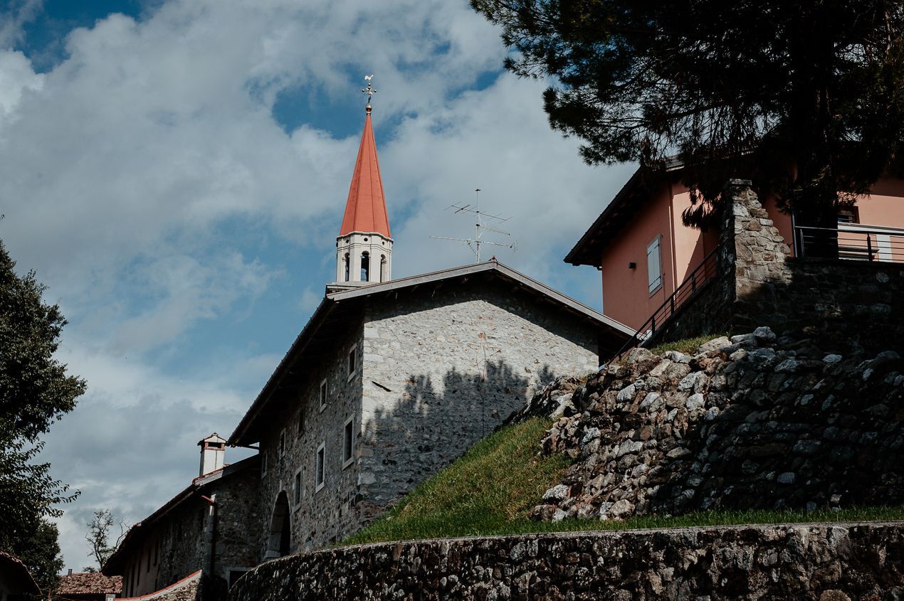 Church building with red spire and stone walls set against cloudy blue sky in European village setting.