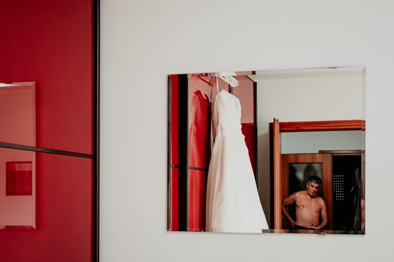 A wedding dress hanging on a red wall with a mirror reflection.