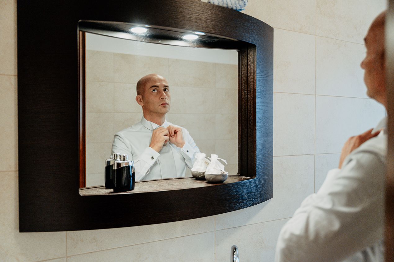 Person adjusting tie while looking in framed bathroom mirror.