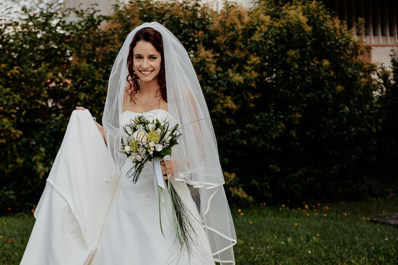 Radiant bride in a classic white wedding dress holding a white and green bouquet outdoors.