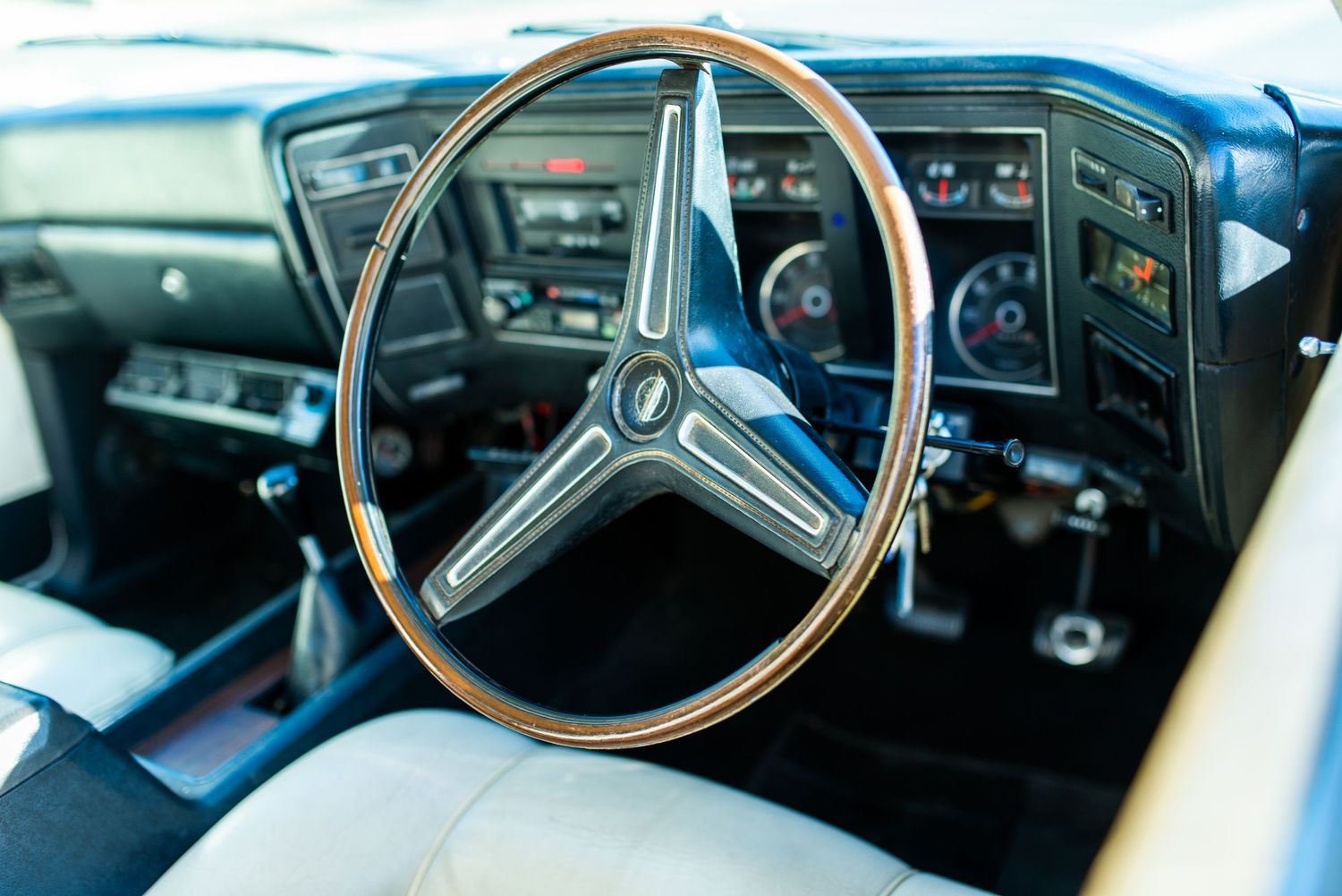 Vintage steering wheel and dashboard gauges in classic car interior.