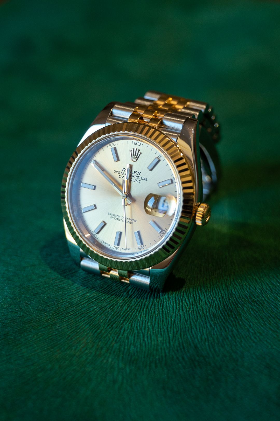 Two-tone Rolex with fluted bezel photographed against emerald green backdrop.