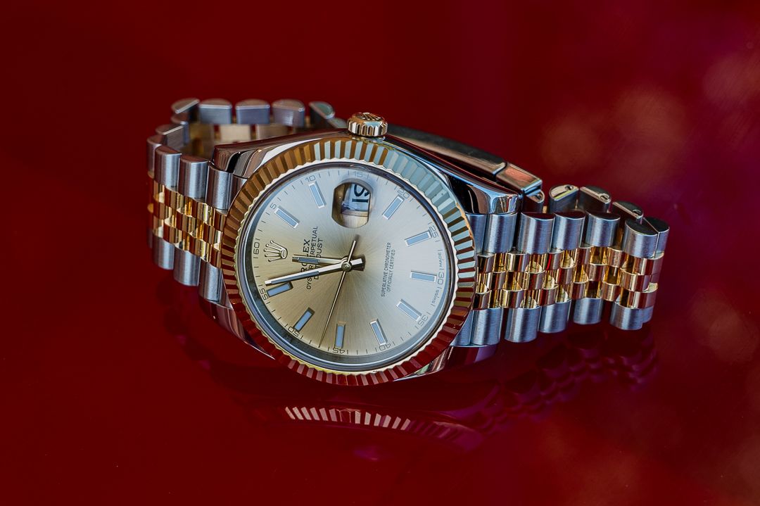 Luxury two-tone Rolex watch with champagne dial photographed on red background.