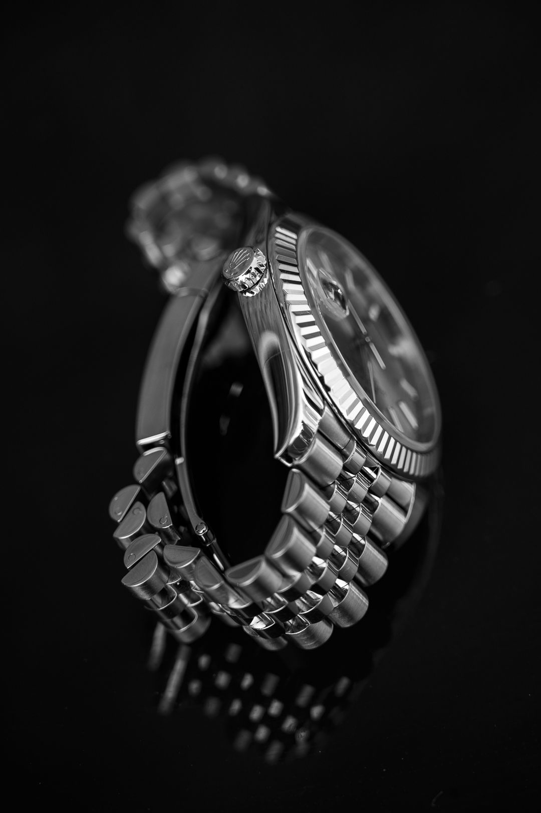 Close-up black and white detail of Rolex watch fluted bezel and bracelet.