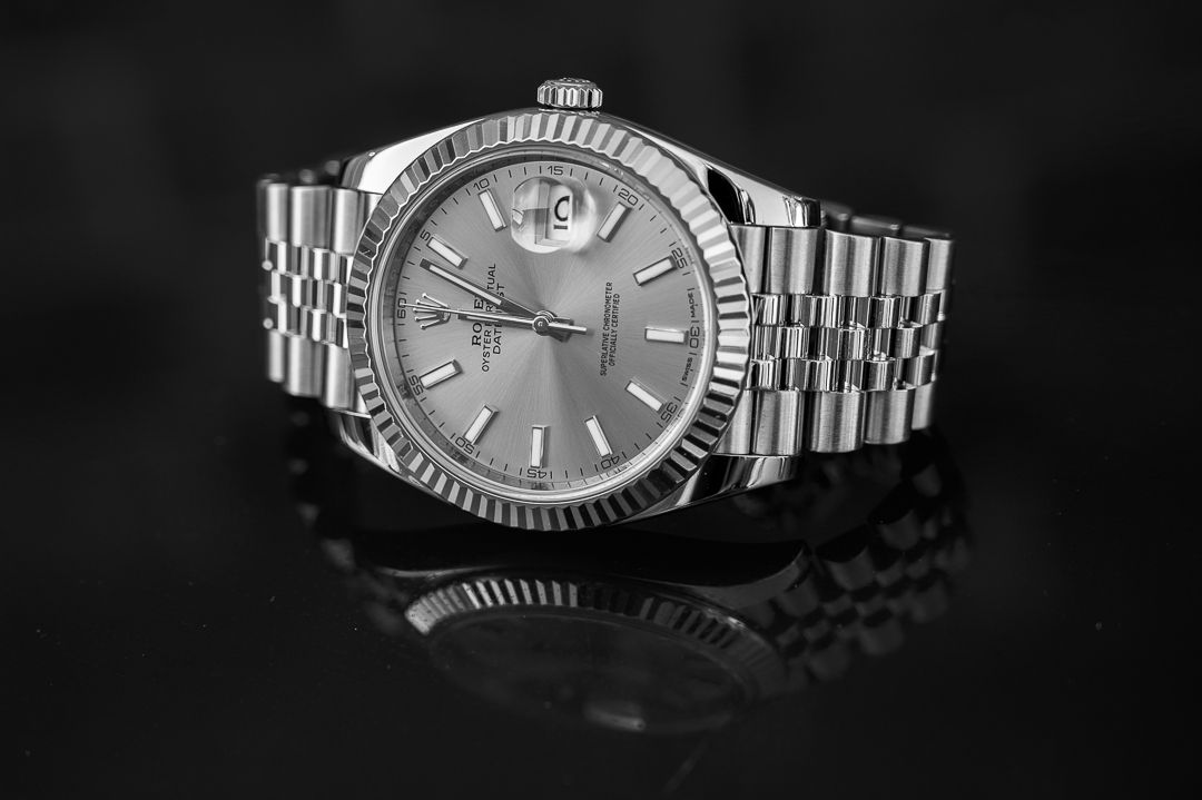 Rolex with silver dial and fluted bezel on reflective black surface.