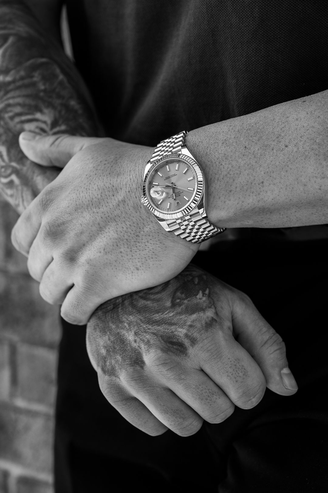 Black and white photo of Rolex watch on tattooed arm.