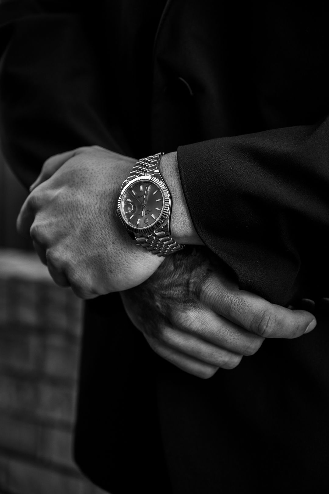 Close-up black and white photo of a luxury watch on a wrist against dark fabric.