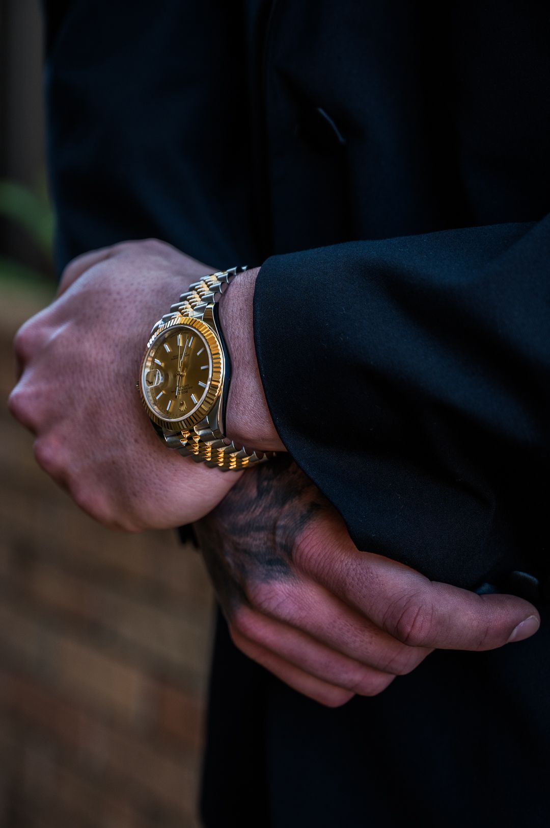Detailed shot of a gold watch on wrist with dark suit sleeve.