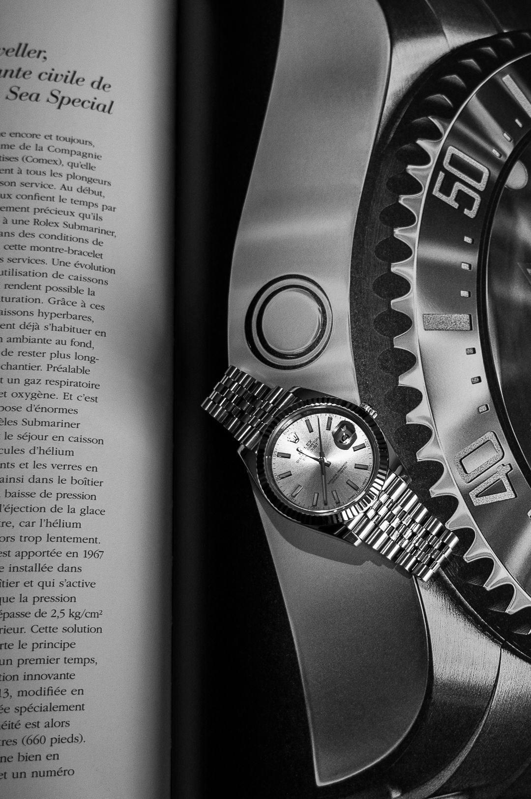 Artistic black and white photo of Rolex watch against printed magazine page.