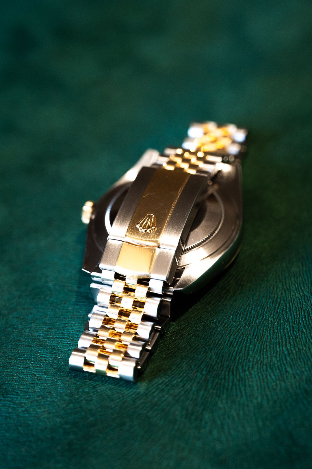 Two-tone Rolex bracelet clasp detail on green leather surface.