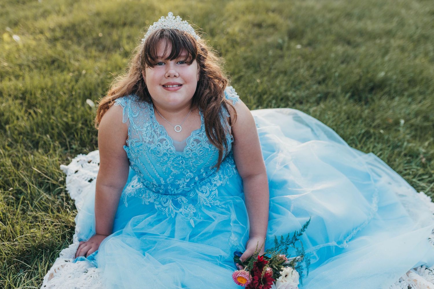 Someone wearing a sparkly blue formal dress sits in a grassy field.