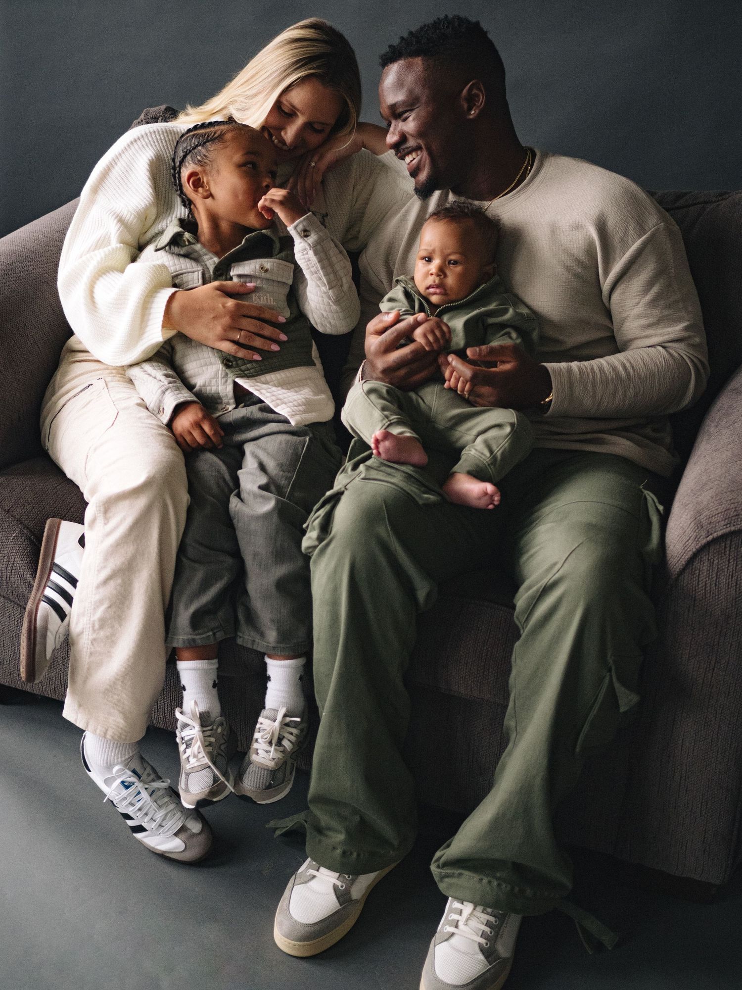 A family shares a joyful moment together on their couch in casual matching outfits.
