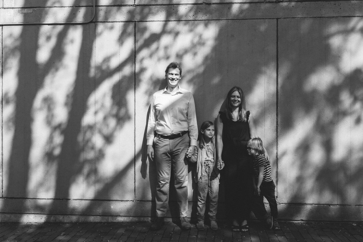 Black and white photo of family standing against wall with dramatic shadow play.