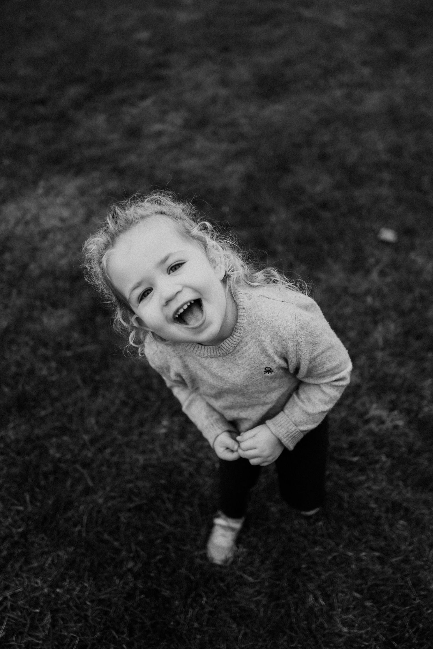 Black and white portrait of joyful child laughing outdoors on grass.